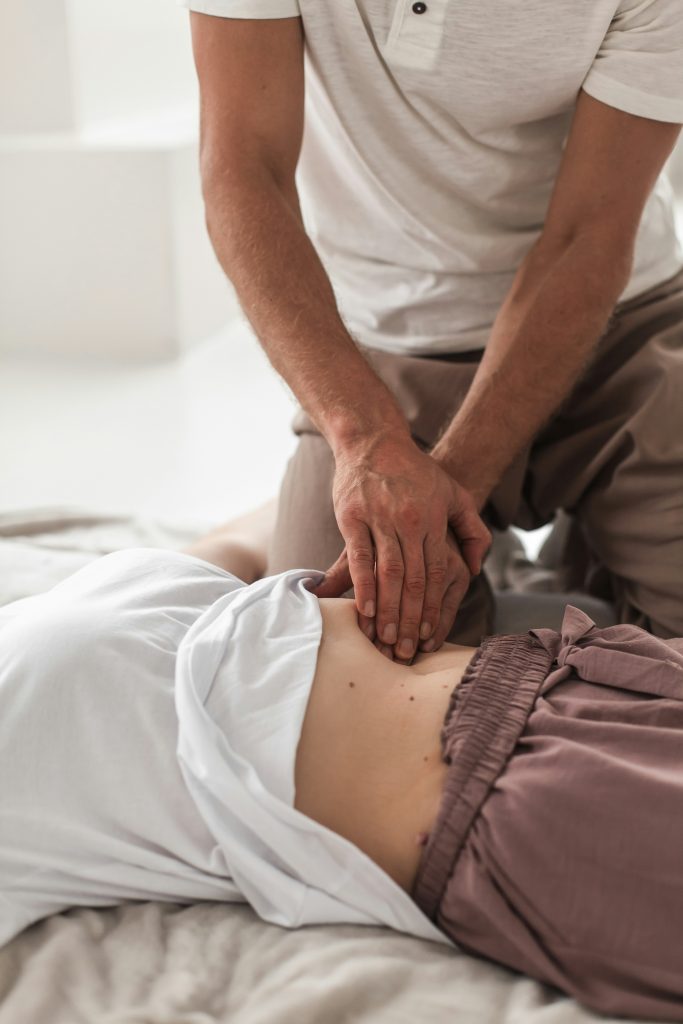 Physiotherapeut führt eine Bauchmassage bei einer liegenden Person durch, um Verspannungen zu lösen und die Gesundheit zu fördern.